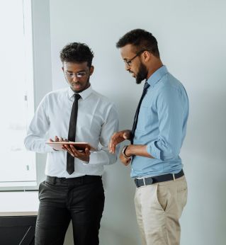 Two businessmen discussing work with a tablet against a white wall in a modern office setting.