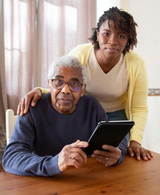 A senior man with eyeglasses and caregiver using a tablet at home, focusing on care and companionship.